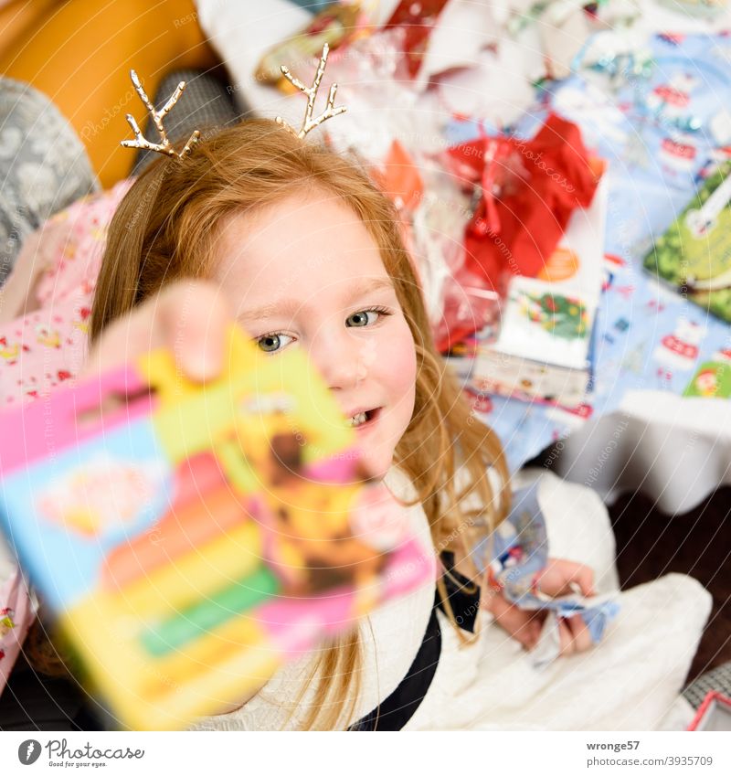 Girl with long reddish blonde hair shows her christmas present to the camera Christmas Christmas gift Giving of gifts Child Long-haired red blonde