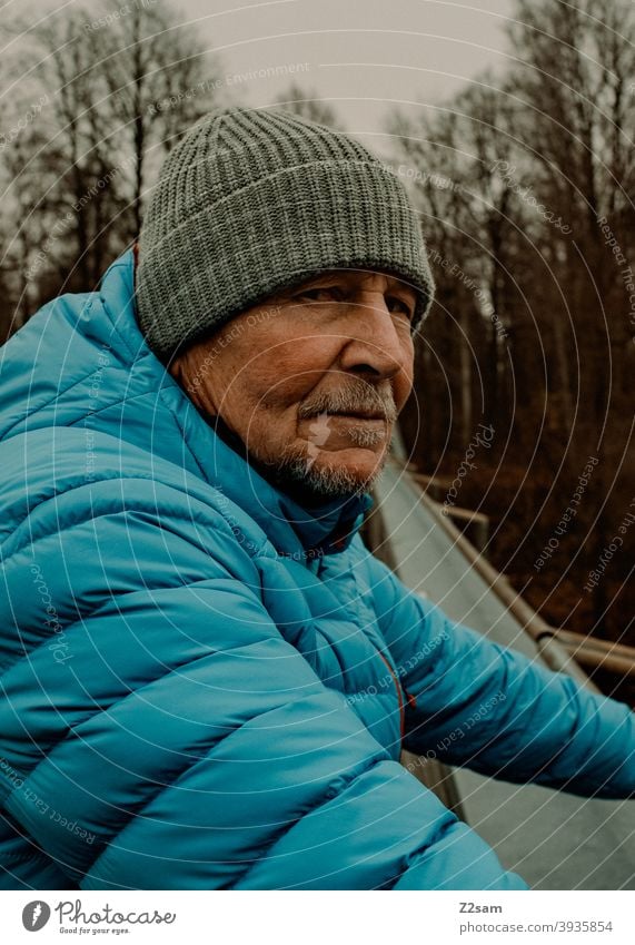 Skeptischer Blick eines sportlichen Rentners in der Natur spazieren natur outtdoor rentner alter mann portrait mütze winter kälte landschaft wald sträucher isar