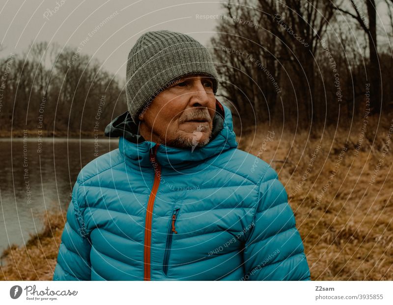 Portrait eines sportlichen Rentners in der Natur spazieren natur outtdoor rentner alter mann portrait mütze winter kälte landschaft wald sträucher isar freizeit