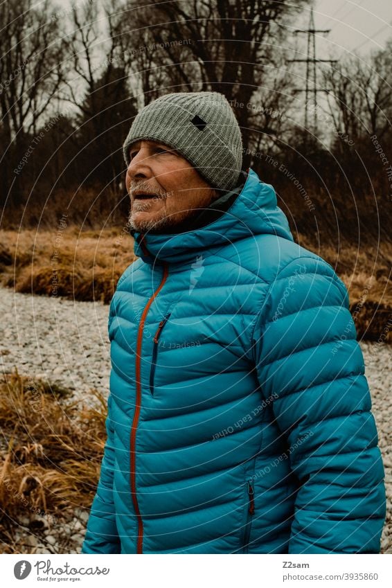 Portrait eines sportlichen Rentners in der Natur spazieren natur outtdoor rentner alter mann portrait mütze winter kälte landschaft wald sträucher isar freizeit