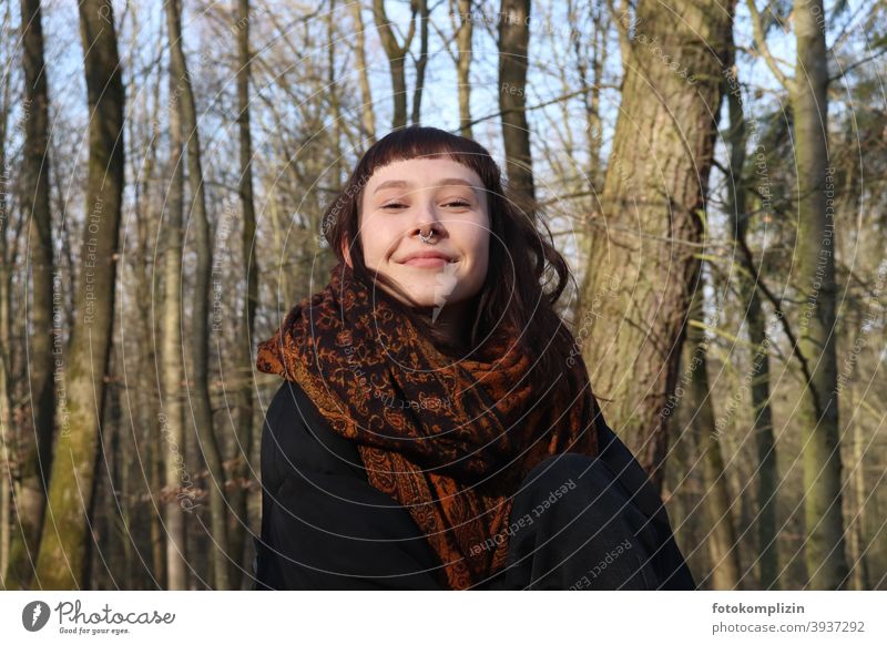 Portrait of young smiling woman with nose piercing under bare trees Young woman Face of a woman smilingly Impish feminine young adults youthful Brunette