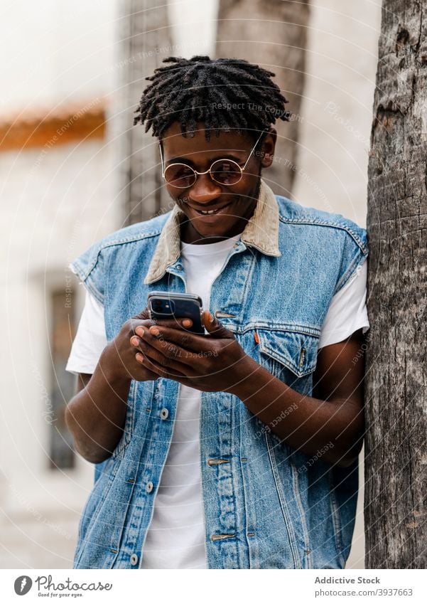 Black man using smartphone on street hipster trendy browsing style gadget afro device young positive african american black denim jeans guy dreadlocks park