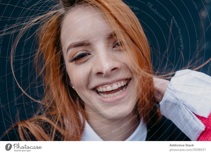 Smiling woman with wind in hair on street redhead flying hair carefree charming red hair enjoy smile female content young ginger cheerful city style positive