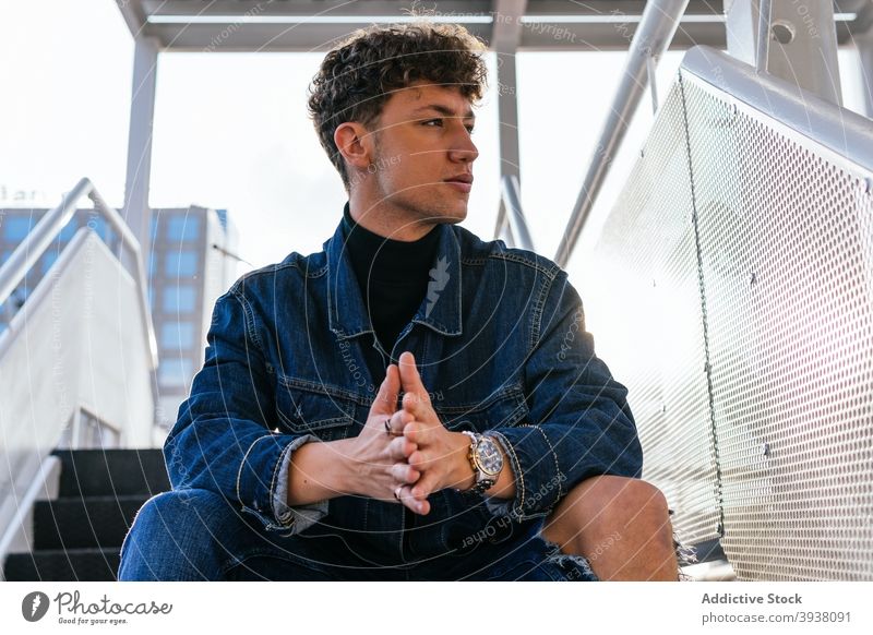 Stylish man sitting on stairs in city denim outfit modern style trendy model serious male staircase street step urban thoughtful relax pensive contemporary guy