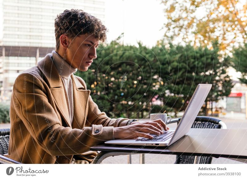 Serious man working on laptop in street cafe freelance typing remote project browsing city male serious focus concentrate device netbook using gadget table job