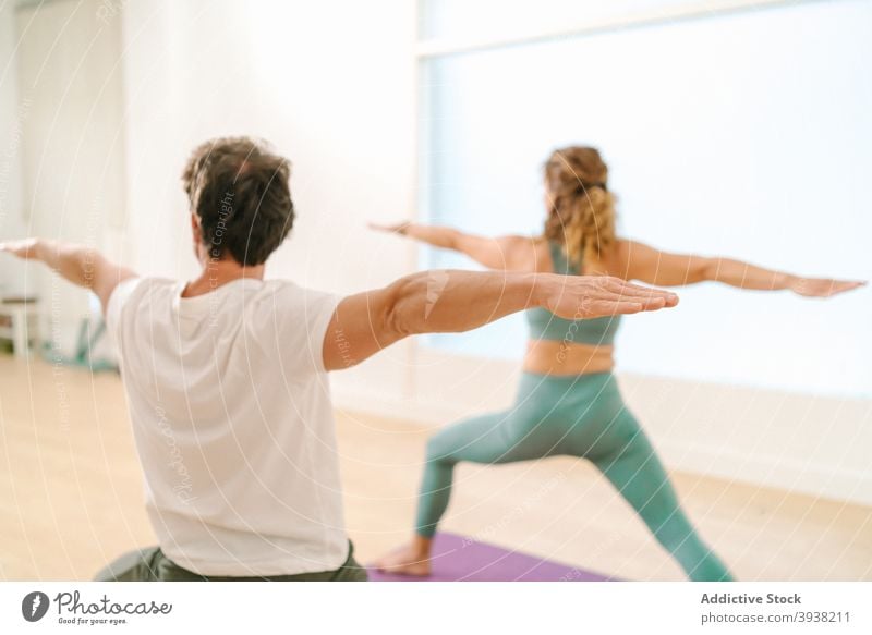 Man and woman doing yoga in Warrior pose in studio warrior pose practice balance together class zen barefoot outstretch arm flexible asana wellness