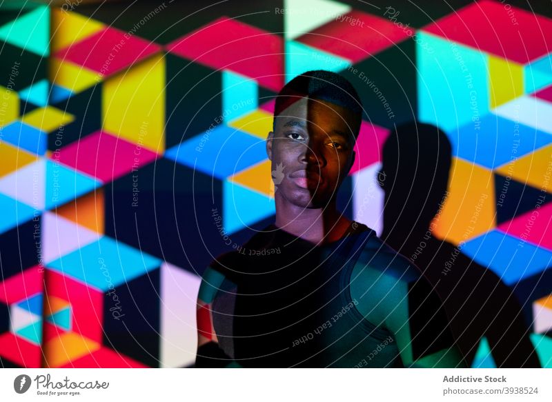 Ethnic man in dark studio with colorful neon illumination light cube geometry illuminate vivid model male black ethnic african american style trendy fashion