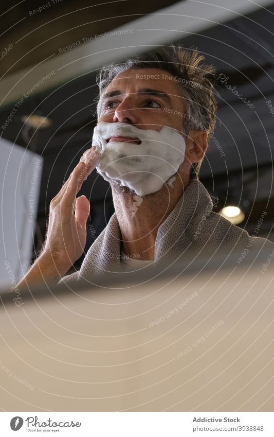 Handsome Man Applying Shaving Cream shave cream applying man middle age reflection mirror bathroom at home shaving skin care front view portrait male grey hair