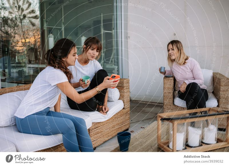 Company of women relaxing together on terrace company friend smartphone watch video friendship gather female meeting cozy house browsing happy cheerful gadget