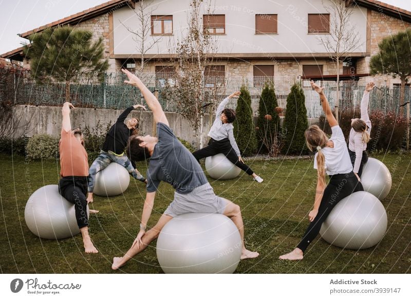 Group of people doing pilates exercises on fit balls group class training side bend together stretch lawn sportswear company wellness wellbeing fitness healthy