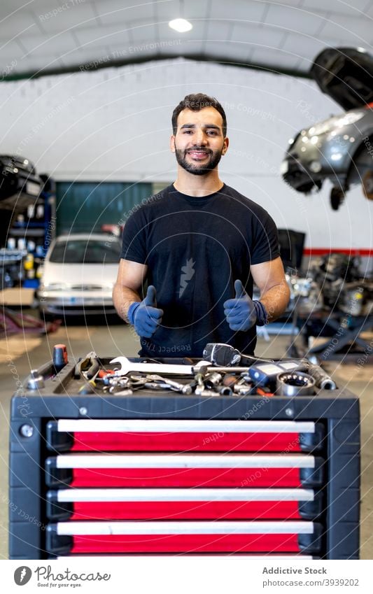 Smiling man with tool cabinet in car service mechanic technician instrument thumb up gesture male various happy job friendly garage maintenance positive work
