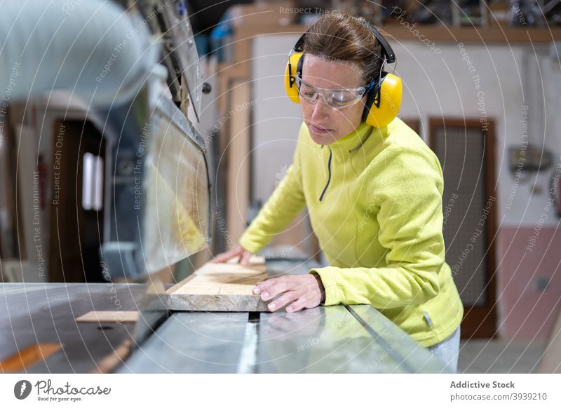 Serious craftswoman working on saw bench machine wood artisan workbench focus joinery workshop occupation wooden board female adult sharp professional job