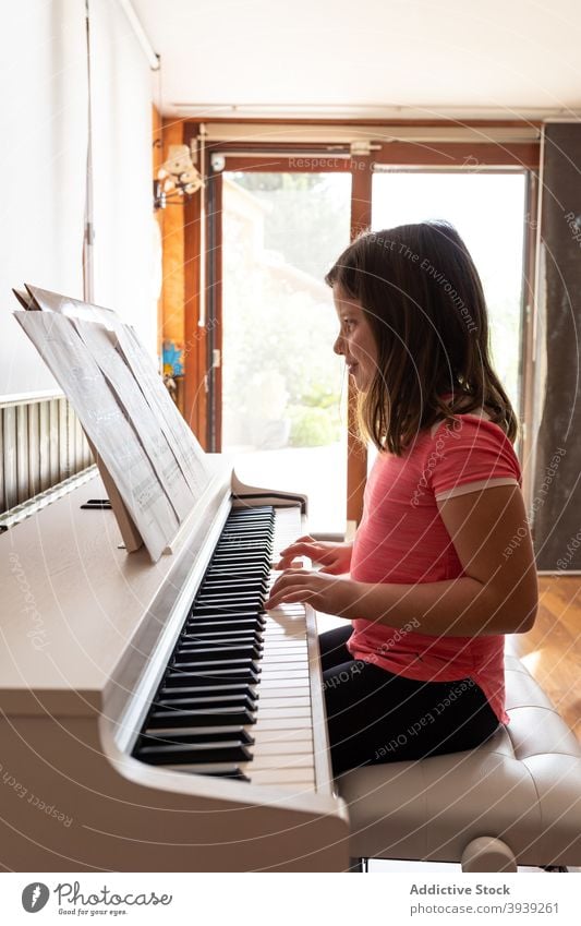 Smiling child playing piano in cozy room in daylight rehearsal read music note musician home instrument positive melody girl kid casual learn adorable acoustic