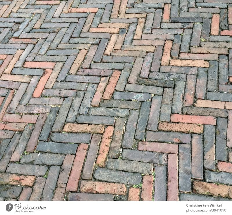 Old and worn grey and reddish paving stones / slips are laid in a herringbone or spike pattern Paving stone stone pavement straps Floor covering Pavement