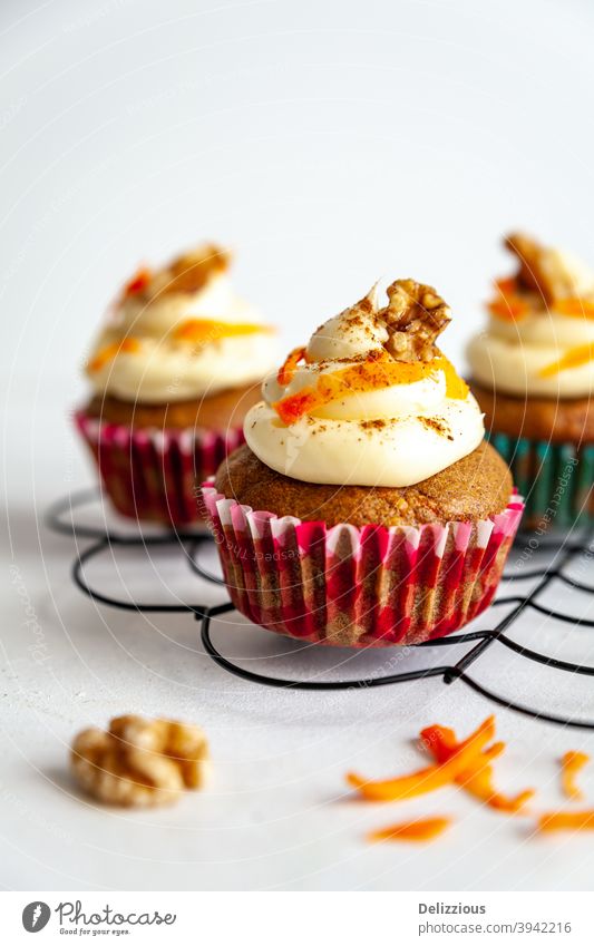 three carrot cake muffin with icing and carrot shaving on cooling rack white background cupcake dessert food sweet baked birthday cupcakes frosting delicious