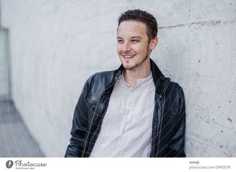 young man, business, leather jacket, outside in front of concrete wall masculine more adult Upper body arms folded Young man Man Friendliness Smiling Positive