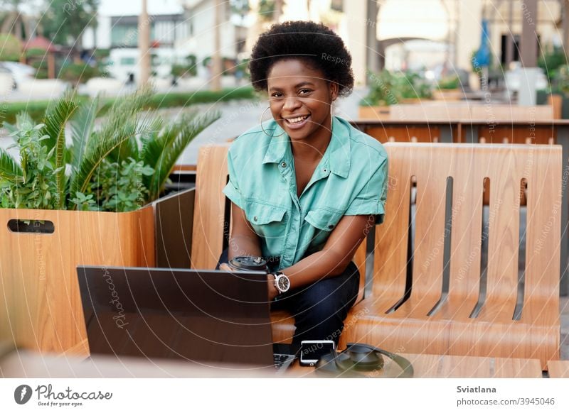 Portrait of a young African girl working at a laptop in a cafe during a coffee break. A break, relax, work online, freelancing woman beautiful bench using happy