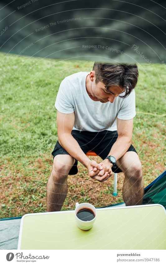 Young man drinking a coffee sitting at front of tent in the morning adventure beverage break breakfast camp camping closeup cup exploration freedom hiker hot