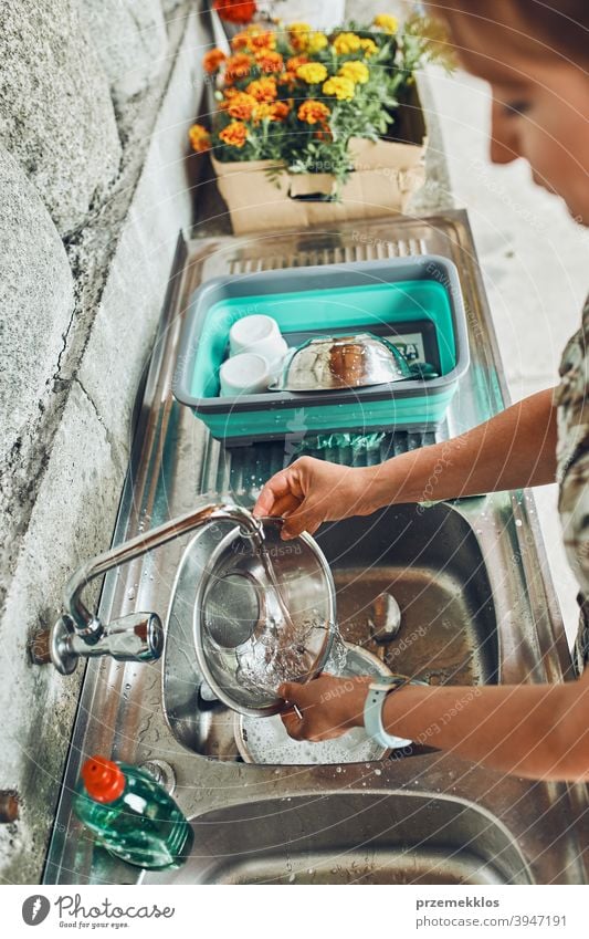 Woman washing up the dishes pots and plates in the outdoor kitchen during vacations on camping campsite cleaning cleanup detergent dirty dish wash dish washing