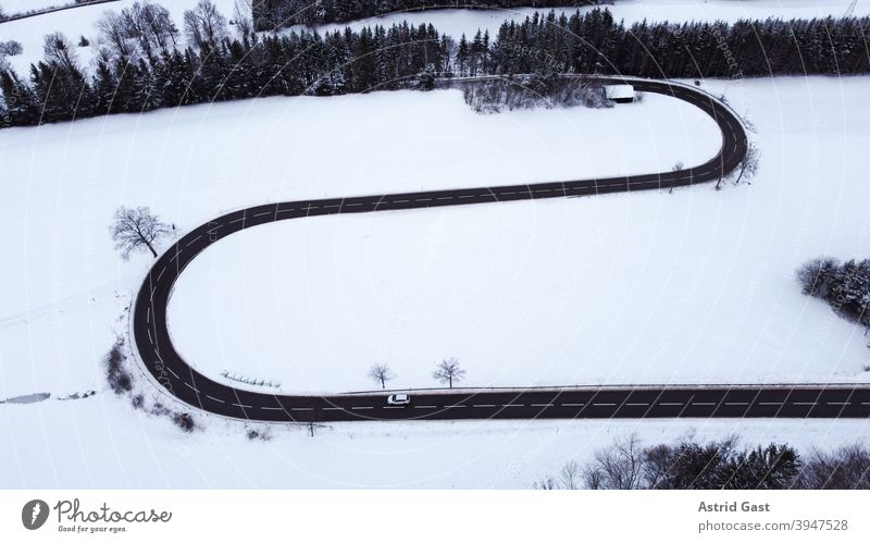 Aerial shot with a drone of a road curve with a moving car in winter Aerial photograph drone photo Winter Street Driving Snow Curve hairpin bend road bend curvy