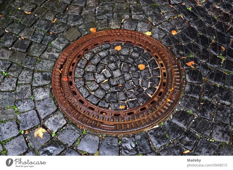 Gully cover with embedded cobblestones with grey paving stones arranged in a circle in pouring rain manhole cover Channel Manhole cover Infrastructure