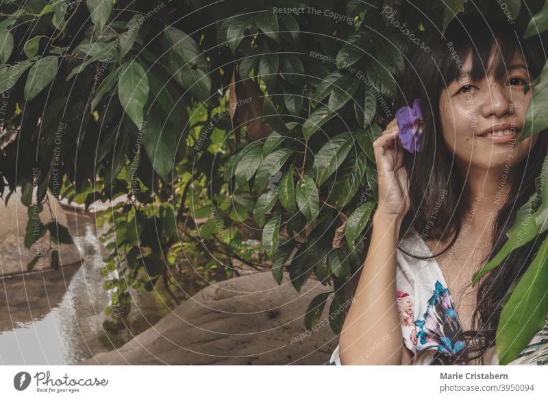 Beautiful woman with flower in her hair against the dark tropical foliage showing concept of Springtime and Summer outdoor person enjoy fun elegant casual