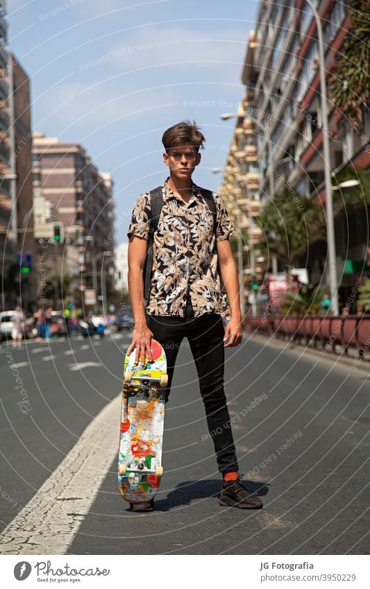 Portrait of young skateboarder man with bad boy face in the middle of the street. portrait guy urban model fashion retro attitude look gaze poster frontal