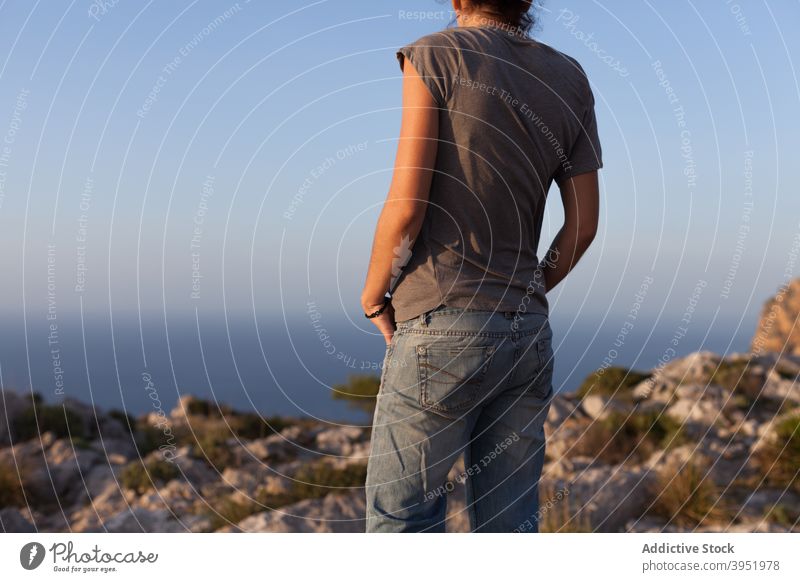 Anonymous female tourist admiring sunset over sea surrounded by mountains standing on hilltop woman relax admire traveler recreation freedom nature landscape