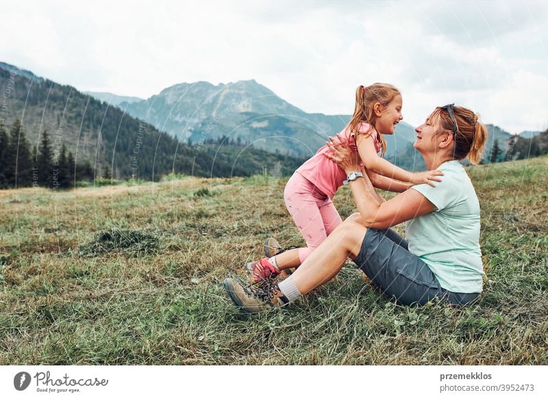 Little girl playing with her mother on grass enjoying summer day during vacation trip in mountains happy excitement enjoyment leisure emotion positive lifestyle