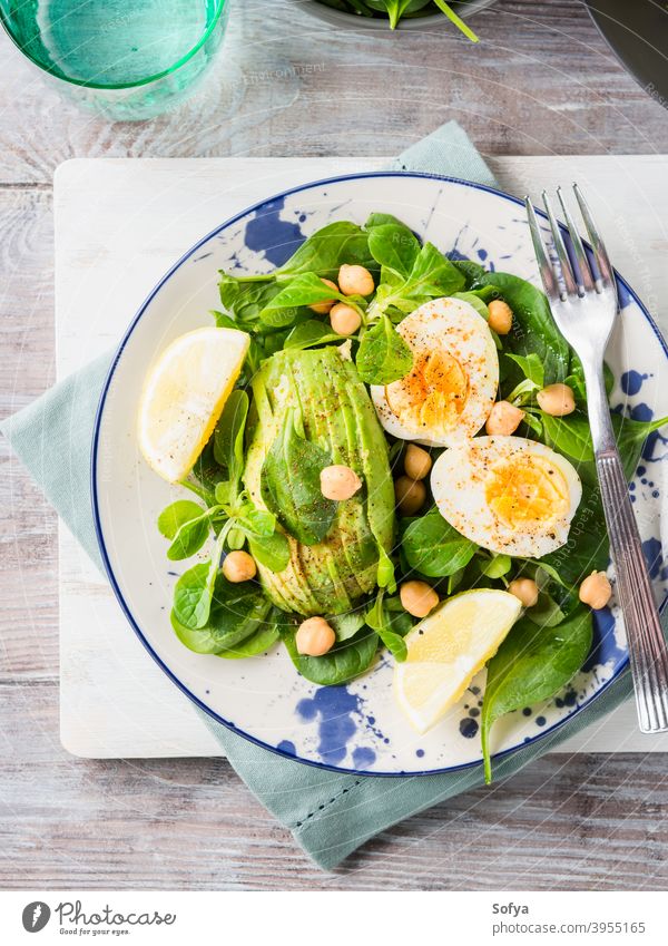 Avocado spinach salad with chickpeas and eggs food avocado vegetable hard boiled cooked served lemon green leaf healthy dish plate wooden nutrition board eat