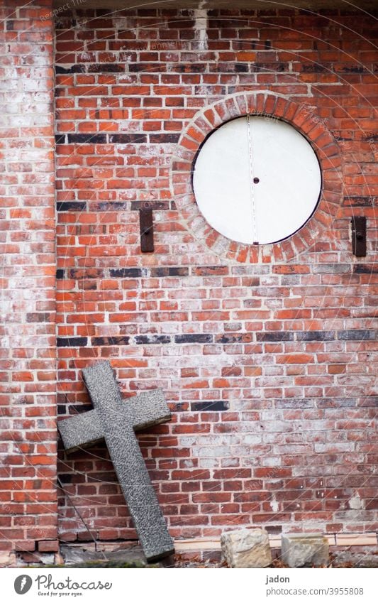 christian cross of stone leans diagonally against a wall, which has a round opening. Religion and faith Crucifix Christian cross Christianity Church