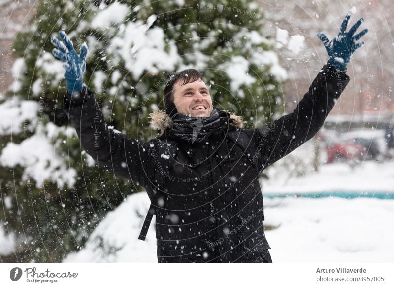 a young man raises his hands towards the sky while it snows. He wears a long black coat pretty Close-up Markets Hooded (clothing) Fashion Happy blow frisky