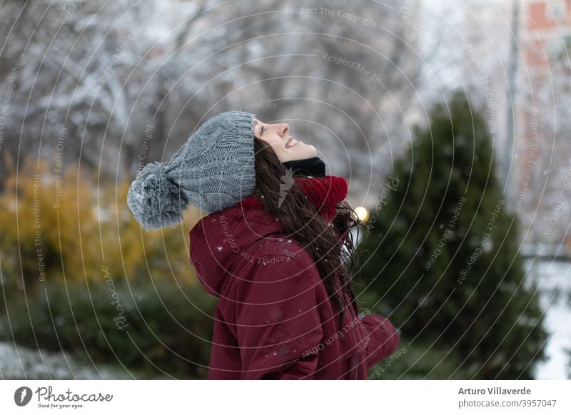 young woman in the snow, wears a gray cap and a red coat. He's smiling looking up at the sky pretty Close-up Markets Hooded (clothing) Fashion Happy blow frisky
