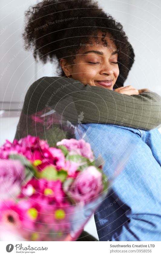 Romantic couple at home with man surprising woman with bunch of flowers celebrating valentines day, birthday or anniversary and she gives him hug young couple