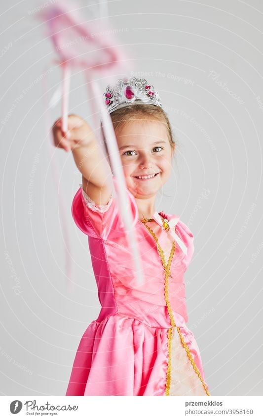Little girl enjoying her role of princess. Adorable cute 5-6 years old girl wearing pink princess dress and tiara holding magic wand fairy child festival