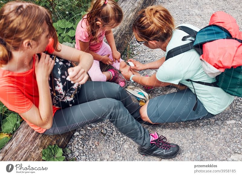 Mother dressing the wound on her little daughters knee with medicine in spray. Accident happened during family summer vacation trip trekking trail foot path