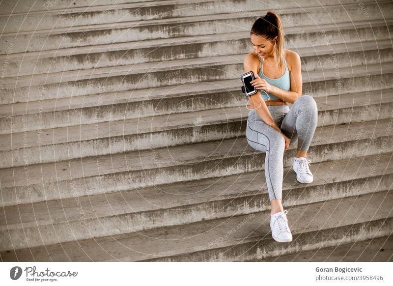 Fitness woman taking a break from running sitting on steps and suing mobile phone in armband young fitness lifestyle urban workout healthy sport training female