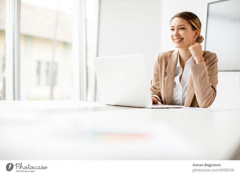 Young woman working on laptop in bright office with big screen behind her adult attractive beautiful business caucasian communication computer confident cute