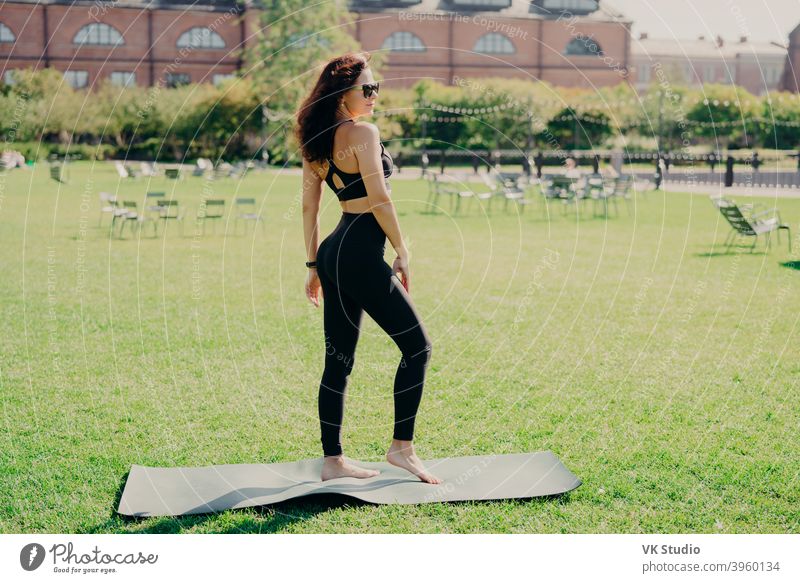 Sporty woman lying on karemat wears activewear raises leg has bare feet  poses on green grass Stock Photo by StudioVK