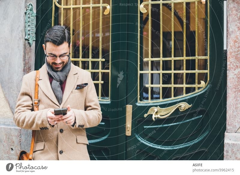 Young elegant man in a retro style using his smartphone at the front door young dandy smart phone cell phone mobile fashion street portrait technology app