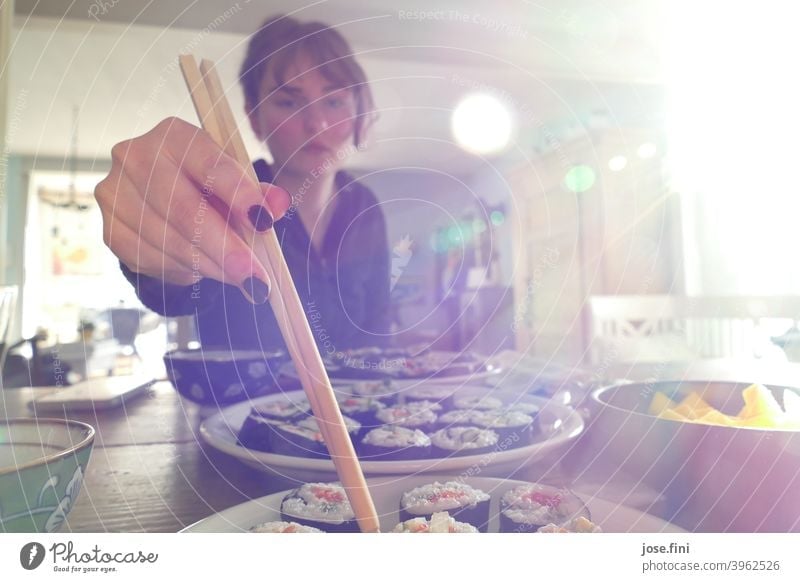 Young woman eating vegetarian homemade sushi, with chopsticks, light coming from right. Japanese Roll Rice Asian traditionally Wasabi Ginger Wooden table