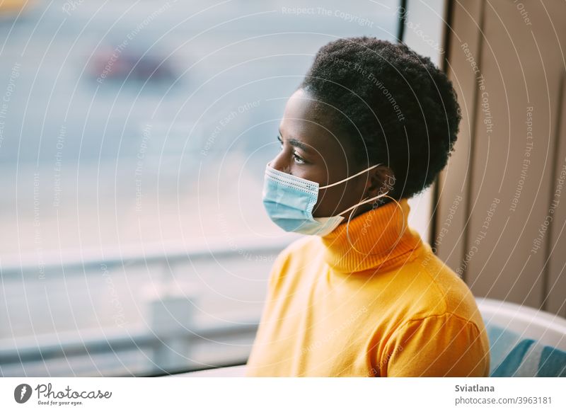 Dubai, UAE, November 2020 A young African woman wearing a protective mask rides on a bus and looks out the window. Coronavirus, social distance. Side view