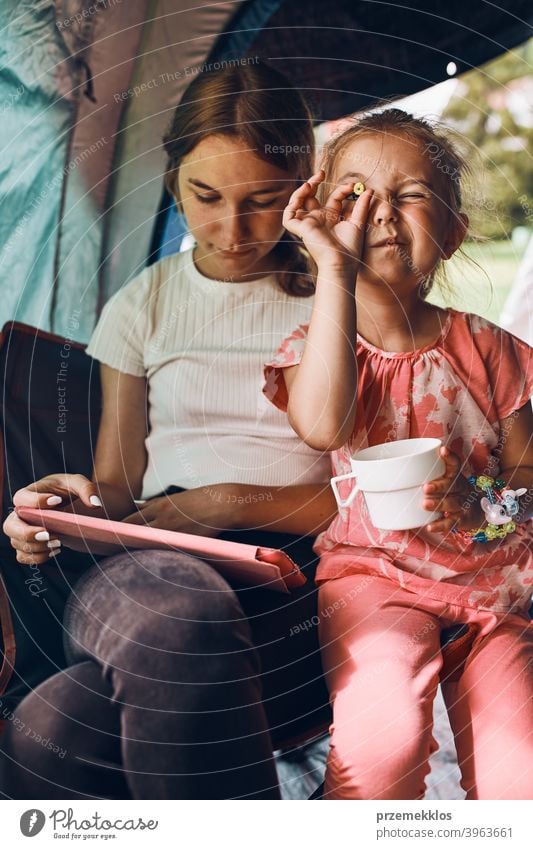 Sisters spending time in a tent on camping. Children using tablet playing games online during summer vacation children girl siblings sister family internet
