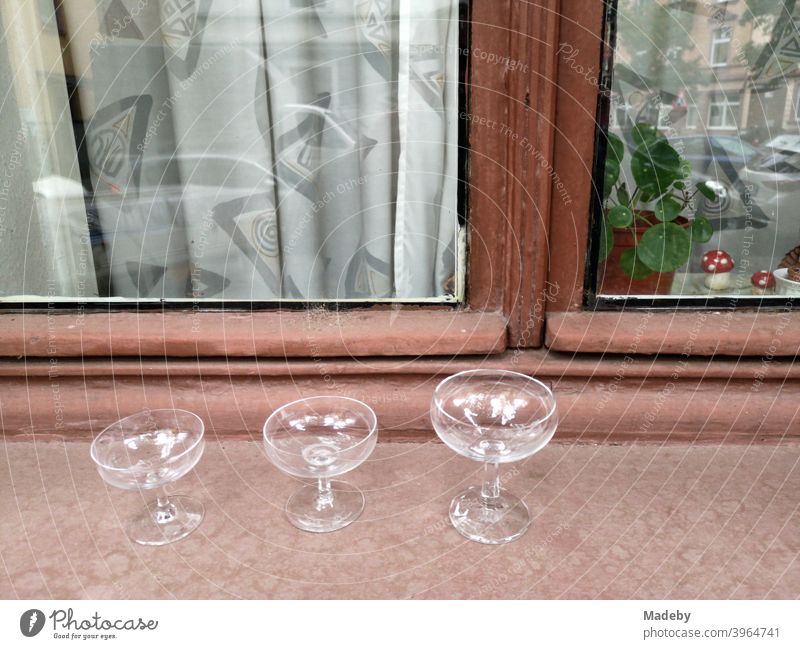 Empty glasses and liqueur bowls on the windowsill of an old building with wooden windows and curtains in the north end of Frankfurt am Main in Hesse, Germany