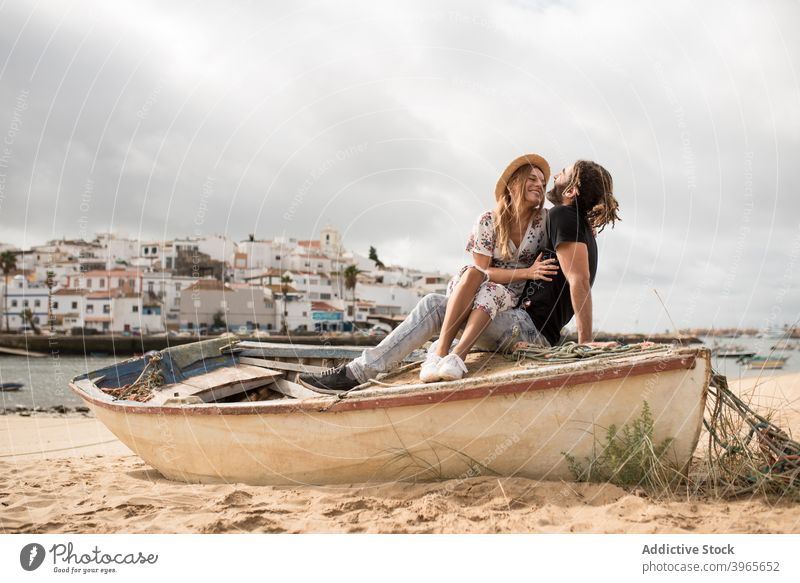 Happy traveling couple hugging on wooden boat on sandy coast against cloudy sky cuddle beach together romantic love smile holiday vacation happy relationship