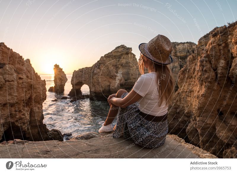 Unrecognizable woman resting near sea and cliffs admire sunset water nature coast stone algarve portugal vacation sit hat ocean travel relax idyllic evening