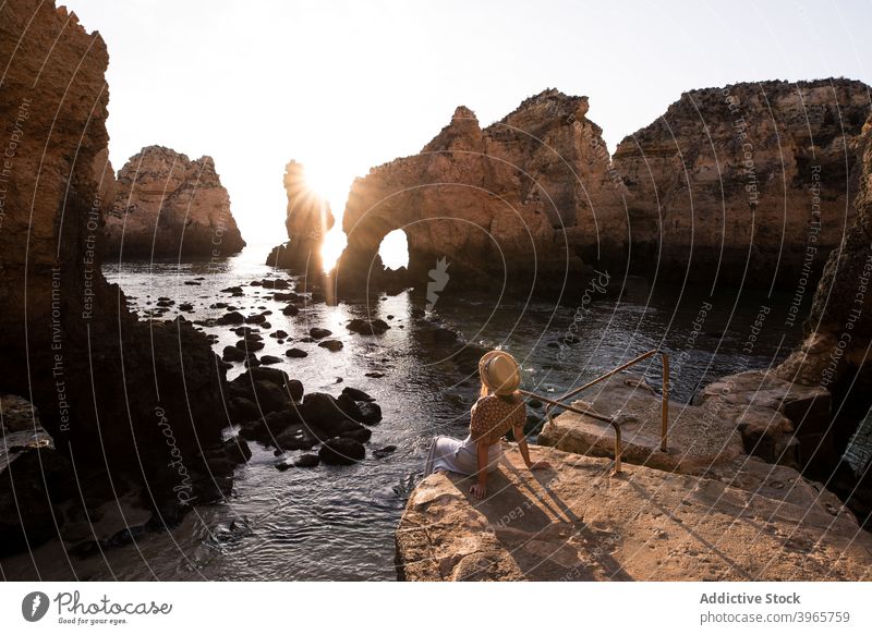 Unrecognizable woman resting near sea and cliffs admire sunset water nature coast stone algarve portugal vacation sit hat ocean travel relax idyllic evening