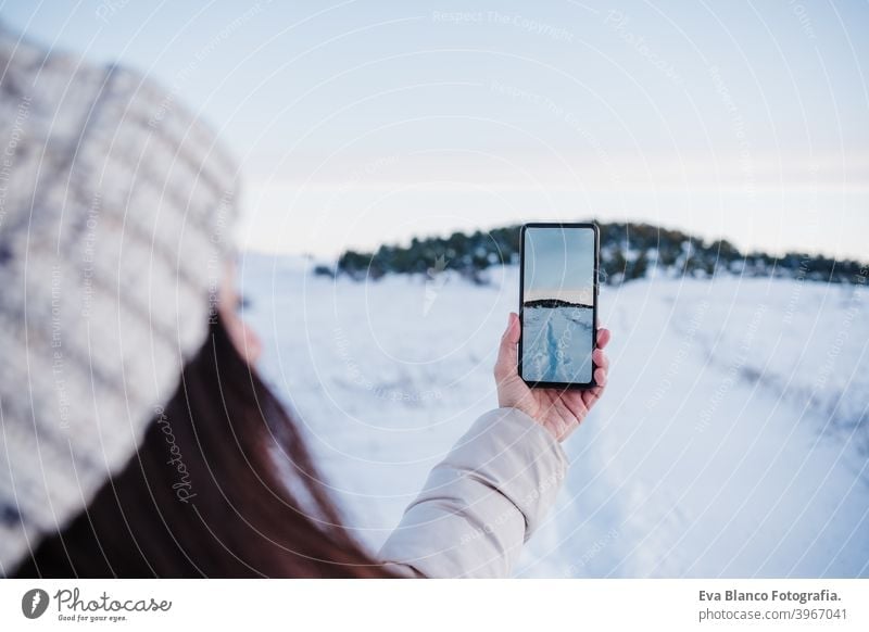 back view of backpacker woman hiking in snowy mountain taking a picture of landscape with mobile phone.winter season. nature and technology sunset cold covered