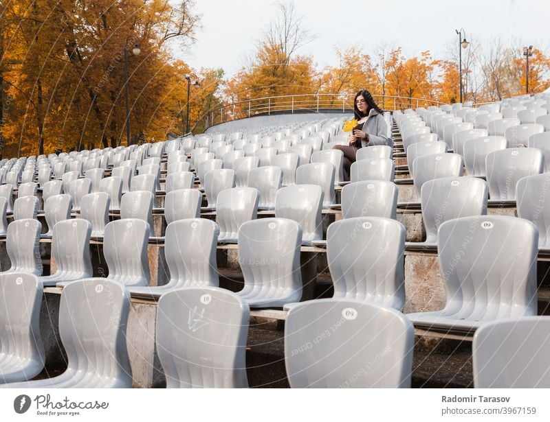 young girl in a gray coat sits on a seat of an empty stadium woman sitting autumn female alone sadness lonely caucasian beautiful emotion outdoor person people