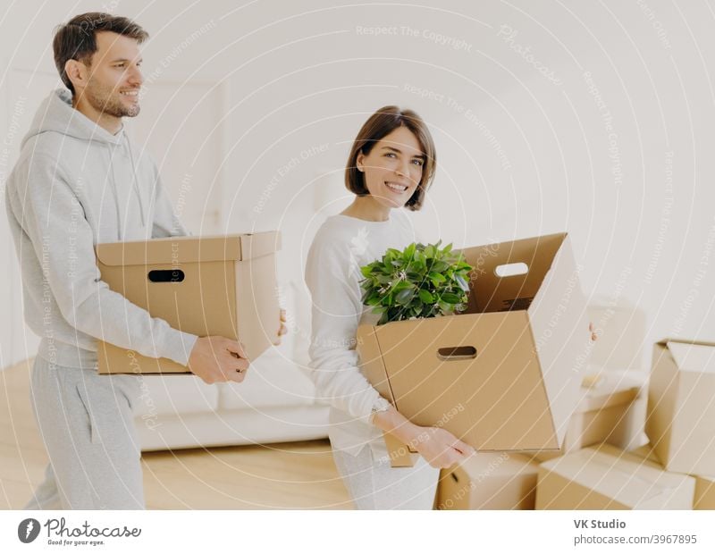 Photo of family couple carry big boxes with households items and personal belongings, move into new home, enter new bought or rented house. Happy homeowners busy with unpacking. Domestic routine